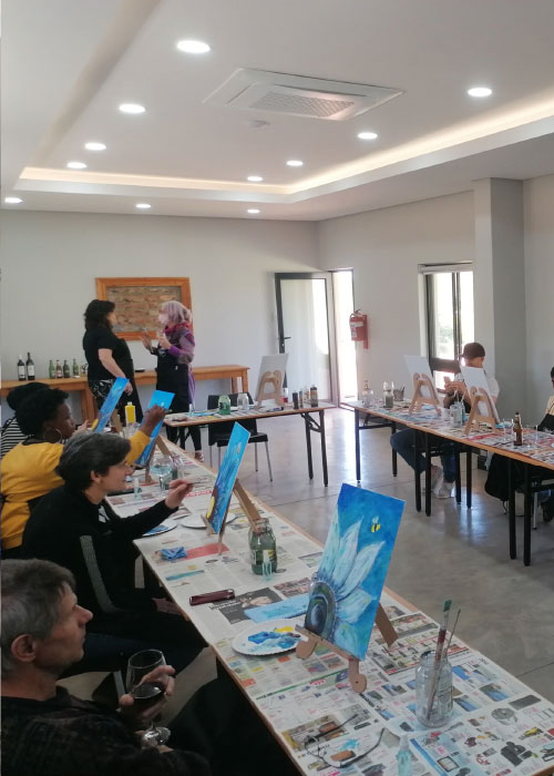 Group art class with guests painting blue-toned canvases at covered tables
