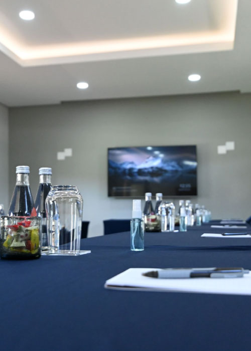 Conference table setup with water bottles, notepads, and wall-mounted screen