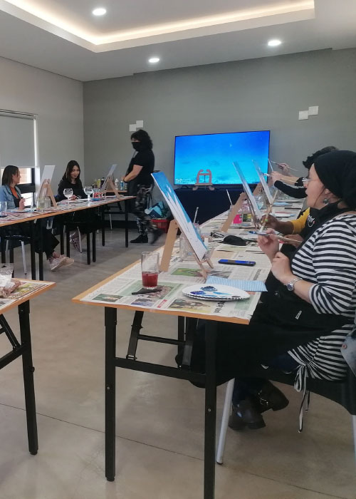 Guests painting on easels during a group art class with reference screen